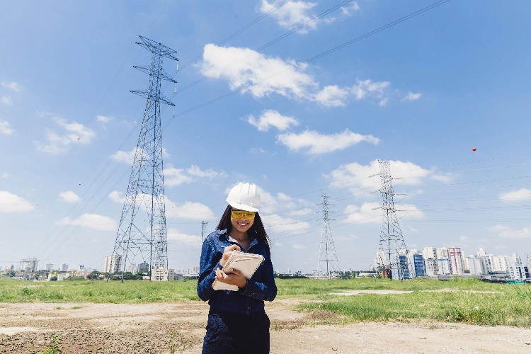 Happy African American Lady Safety Helmet Taking Notes Near High Voltage Line@2X